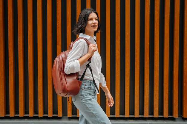 Una joven guapa camina por la calle mientras sostiene una mochila de cuero