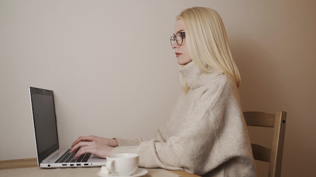 Joven guapa caucásica escribiendo y trabajando en la computadora portátil como autónomo mientras está sentado en casa