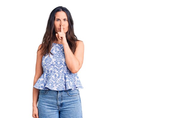 Joven guapa morena con camiseta informal pidiendo silencio con el dedo en los labios. silencio y concepto secreto.