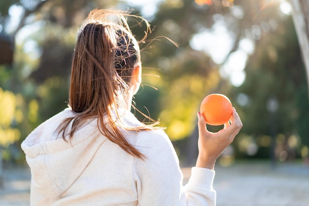 Joven guapa morena sosteniendo una naranja al aire libre en posición trasera