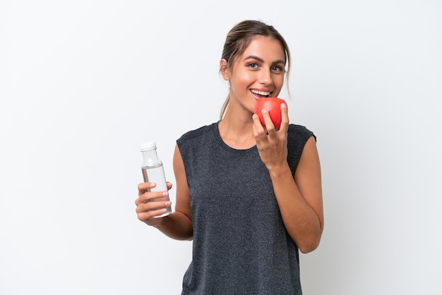 Joven guapa uruguaya aislada de fondo blanco con una botella de agua y comiendo una manzana