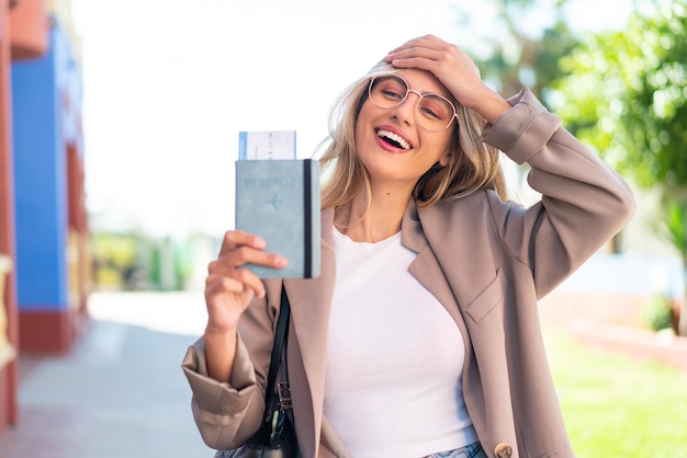 Joven guapa uruguaya rubia al aire libre sosteniendo un pasaporte con expresión sorprendida