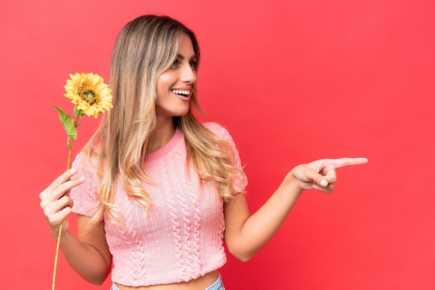 Joven guapa uruguaya sosteniendo girasol aislado en el fondo apuntando hacia un lado para presentar un producto