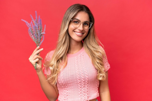 Joven guapa uruguaya sosteniendo lavanda aislada de fondo rojo sonriendo mucho