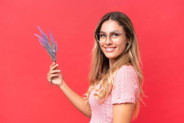 Joven guapa uruguaya sosteniendo lavanda aislada de fondo rojo sonriendo mucho