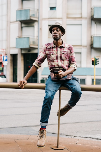 joven guapo afro negro sentado en una barandilla fuera de la ciudad