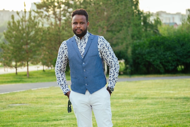 Un joven y guapo afroamericano con un elegante traje en un parque de verano. hombre de negocios negro caminando después del trabajo en la oficina.