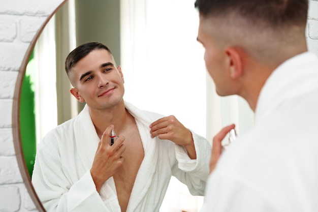 Un joven guapo aplicando perfume en el baño.