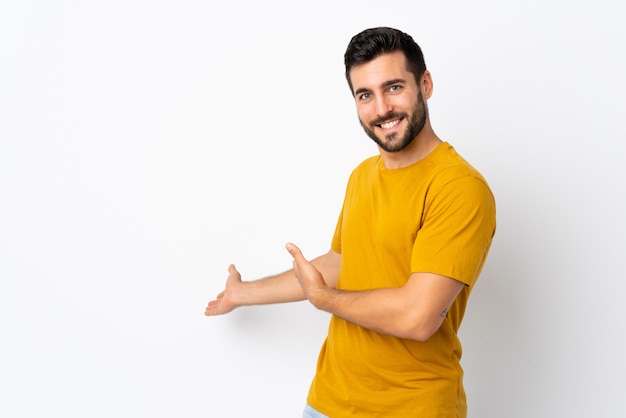 Joven guapo con barba aislado en blanco extendiendo las manos a un lado para invitar a venir