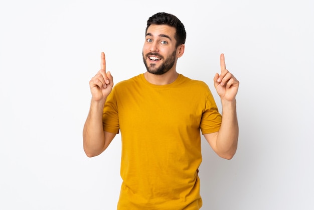 Joven guapo con barba aislado en la pared blanca apuntando hacia una gran idea