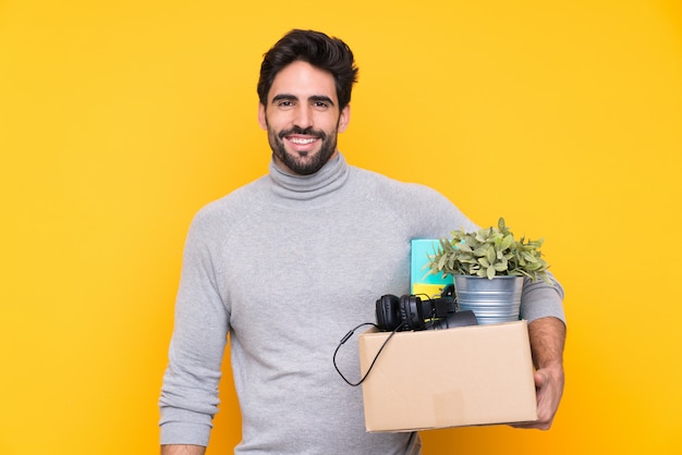 Joven guapo con barba haciendo un movimiento mientras recogía una caja llena de cosas sobre una pared aislada con expresión feliz