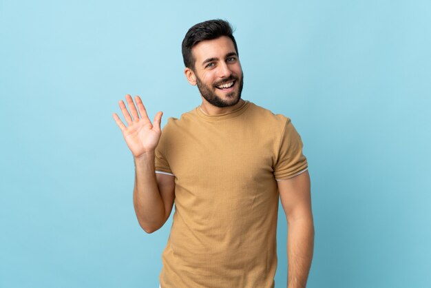 Joven guapo con barba saludando con la mano con expresión feliz