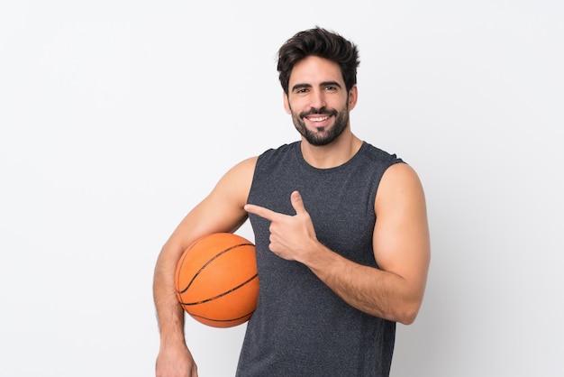 Joven guapo con barba sobre pared blanca aislada jugando baloncesto y apuntando hacia el lateral