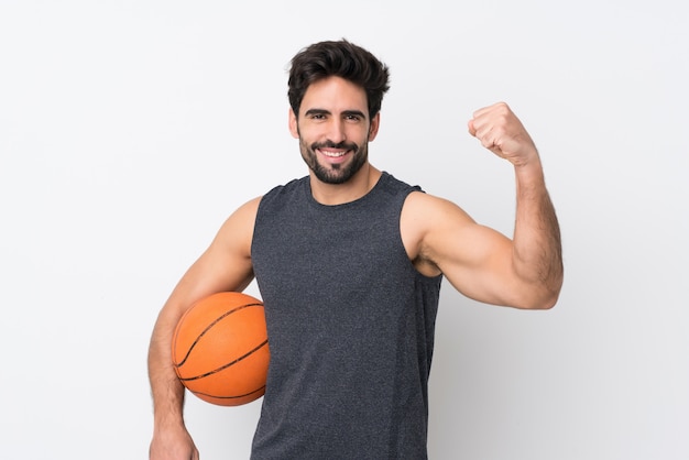 Joven guapo con barba sobre pared blanca aislada jugando baloncesto y orgulloso de sí mismo