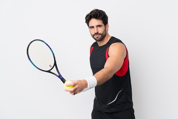 Joven guapo con barba sobre pared blanca aislada jugando tenis