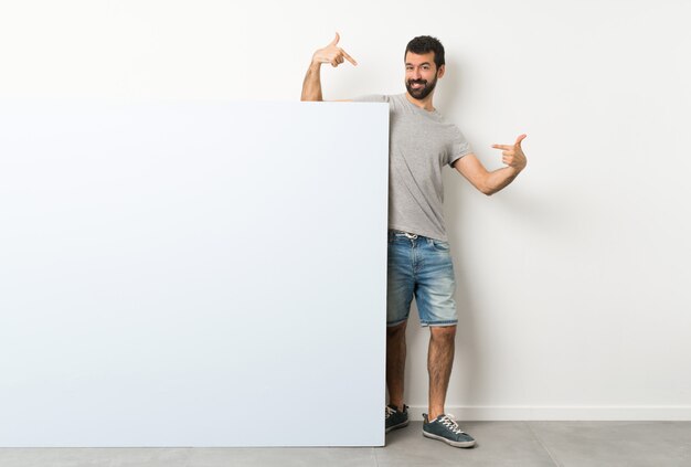 Foto joven guapo con barba sosteniendo un gran cartel vacío orgulloso y satisfecho de sí mismo