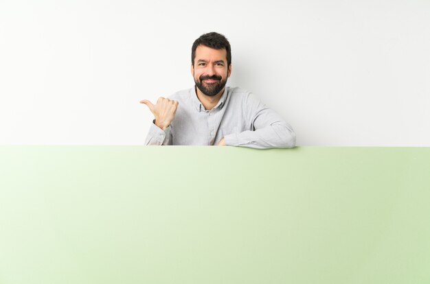 Joven guapo con barba sosteniendo un gran cartel verde vacío