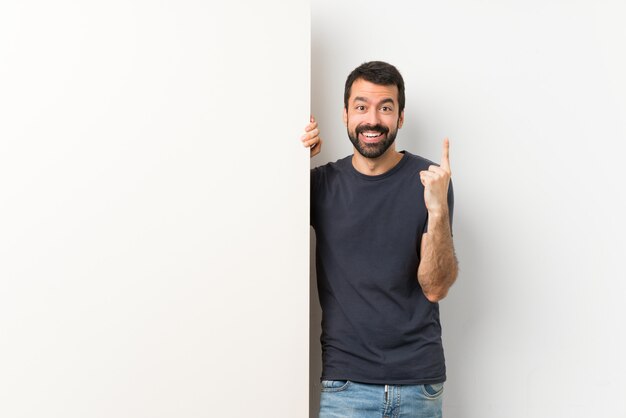 Joven guapo con barba sosteniendo una gran pancarta vacía apuntando hacia una gran idea