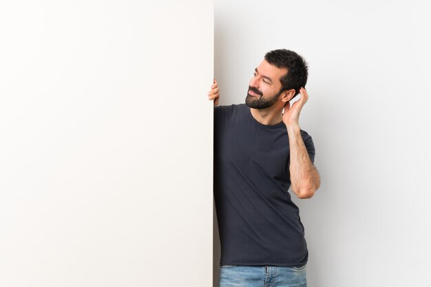 Joven guapo con barba sosteniendo una gran pancarta vacía pensando en una idea