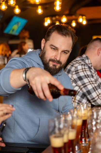 Un joven guapo con barba vertiendo cerveza de botella en vasos