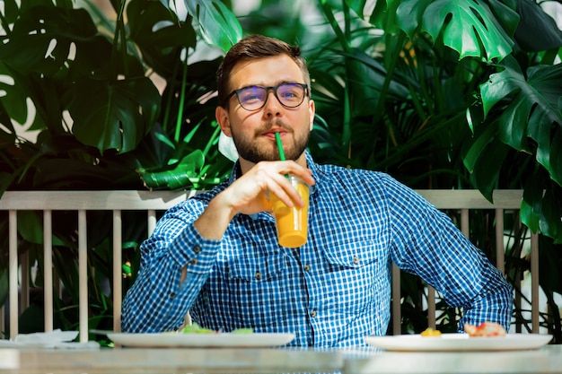 Joven guapo bebiendo jugo en un café