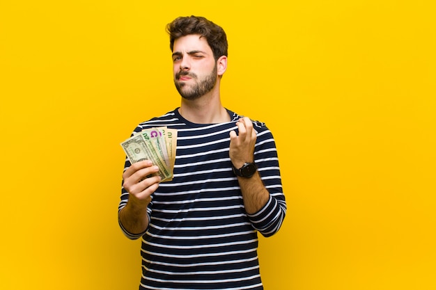 Joven guapo con billetes de dólar contra naranja