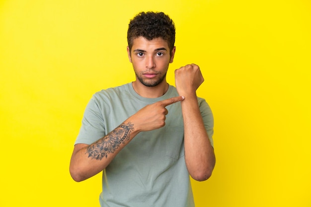 Joven guapo brasileño aislado sobre fondo amarillo haciendo el gesto de llegar tarde