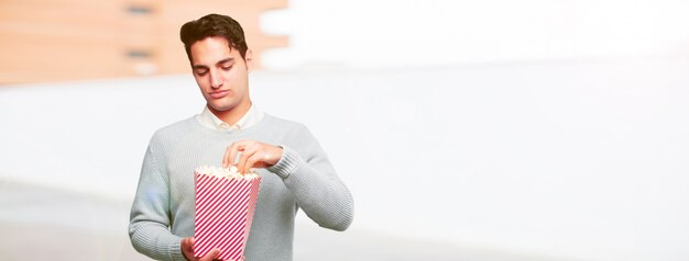 Joven guapo bronceado hombre con un cubo de maíz pop