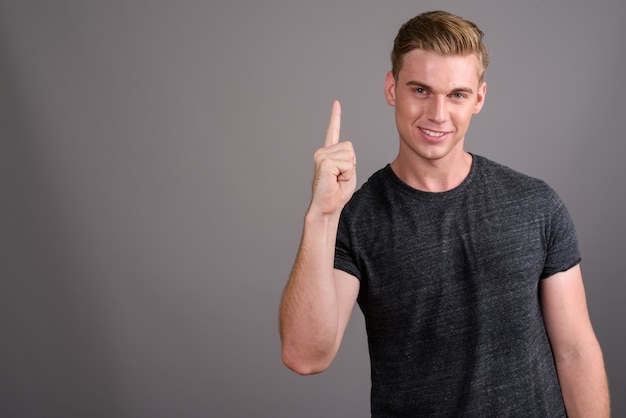 Joven guapo con cabello rubio con camisa gris en la pared gris