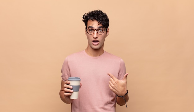 Joven guapo con un café sintiéndose feliz, sorprendido y orgulloso