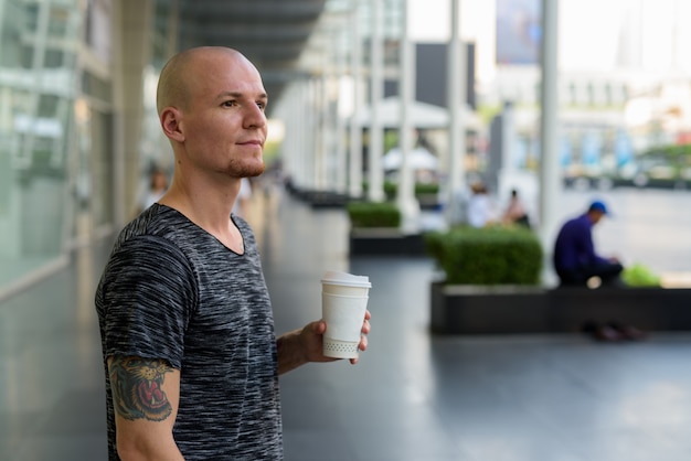 Joven guapo calvo pensando mientras sostiene la taza de café de papel