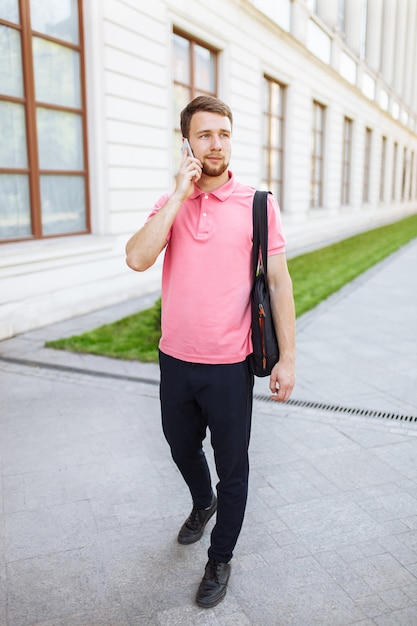 Joven guapo caminando por la ciudad y hablando por teléfono, hipster