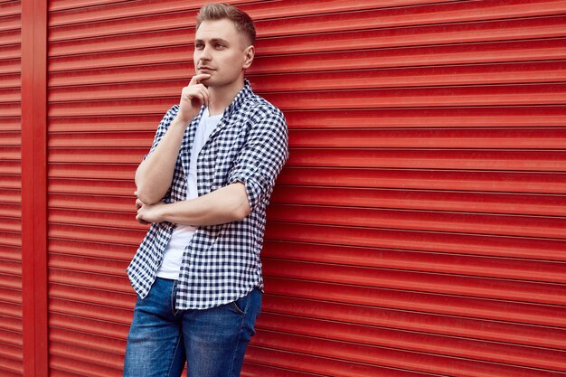 Joven guapo en una camisa y jeans cerca de la puerta roja