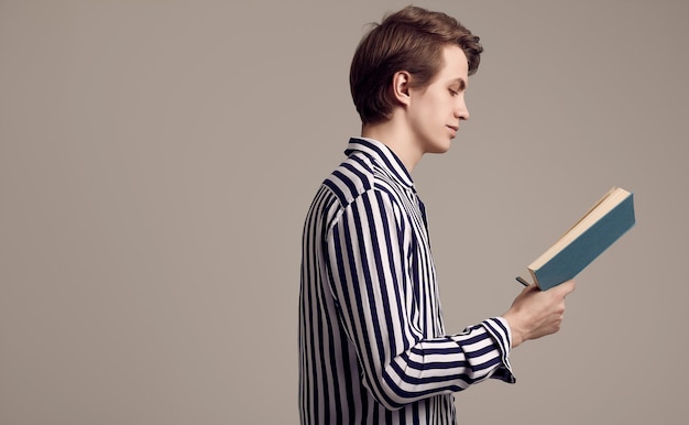 Joven guapo en camisa a rayas leyendo un libro sobre fondo gris
