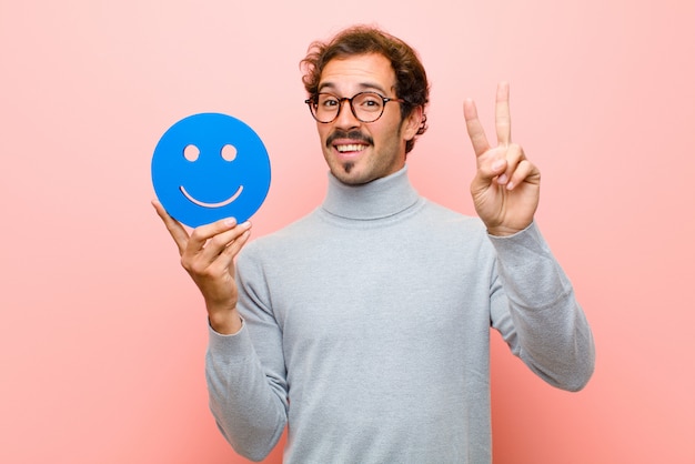 Joven guapo con una cara sonriente contra la pared plana rosa