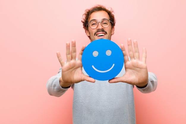 Foto joven guapo con una cara sonriente contra la pared plana rosa