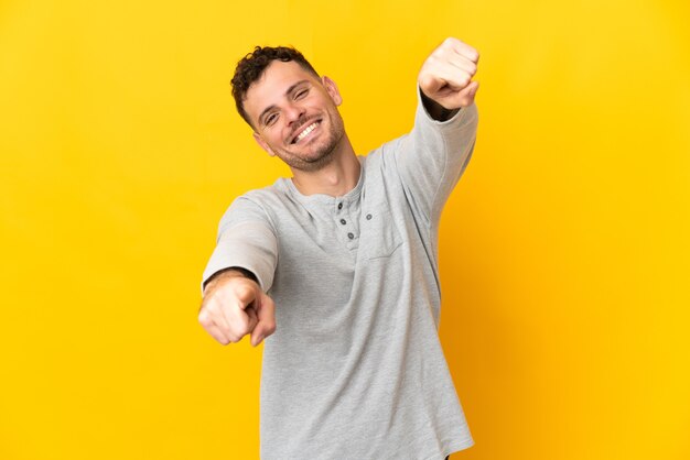 Joven guapo caucásico aislado en la pared amarilla apuntando al frente con expresión feliz