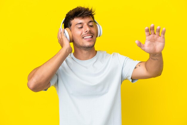 Joven guapo caucásico aislado sobre fondo amarillo escuchando música y bailando