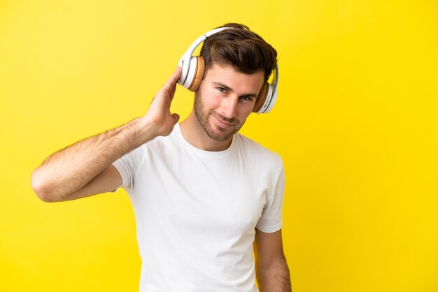 Joven guapo caucásico aislado sobre fondo amarillo escuchando música