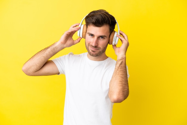 Joven guapo caucásico aislado sobre fondo amarillo escuchando música