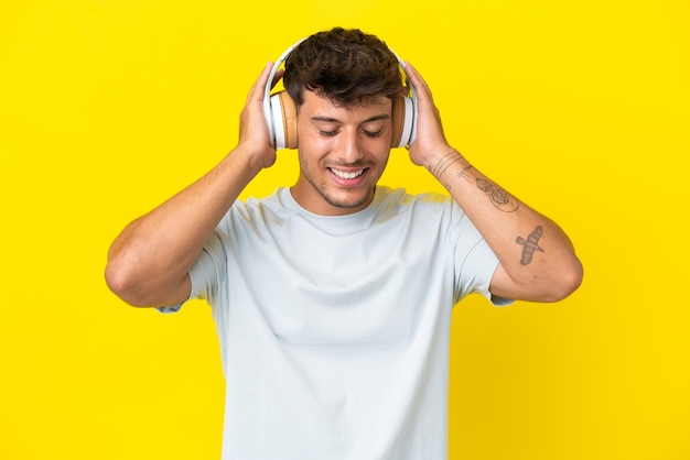 Joven guapo caucásico aislado sobre fondo amarillo escuchando música