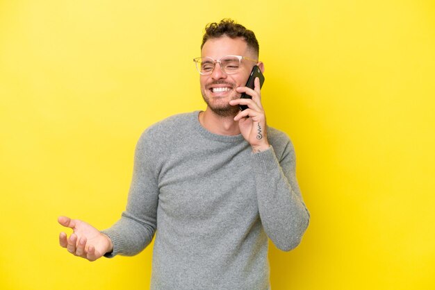 Foto joven guapo caucásico aislado sobre fondo amarillo manteniendo una conversación con el teléfono móvil con alguien