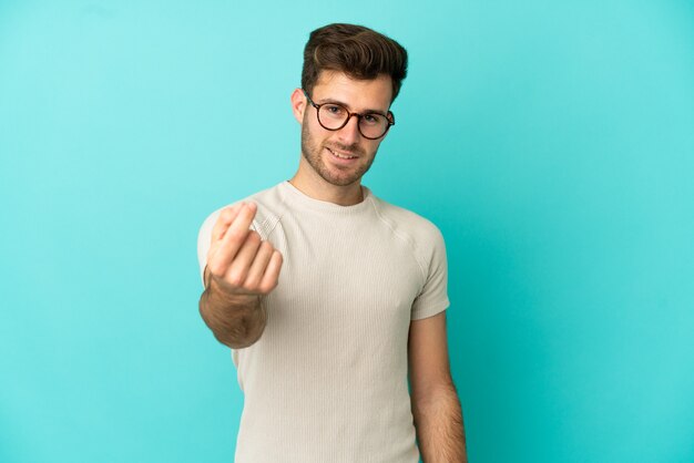 Joven guapo caucásico aislado sobre fondo azul haciendo gesto de dinero