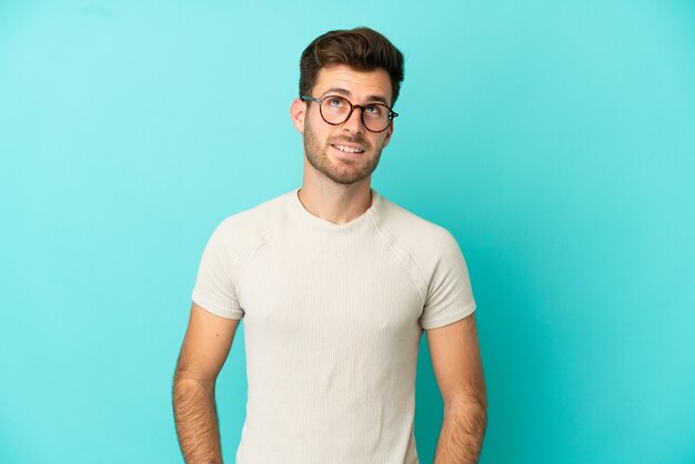 Joven guapo caucásico aislado sobre fondo azul pensando en una idea mientras mira hacia arriba