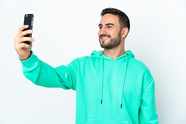 Joven guapo caucásico aislado sobre fondo blanco haciendo un selfie con teléfono móvil