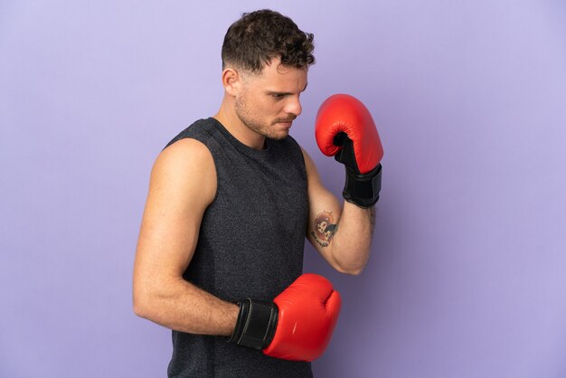 Joven guapo caucásico aislado sobre fondo púrpura con guantes de boxeo