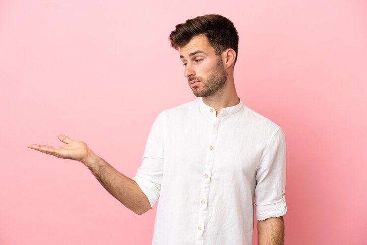 Foto joven guapo caucásico aislado sobre fondo rosa con copyspace con dudas