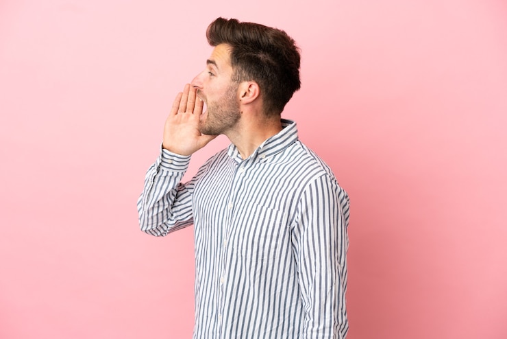 Foto joven guapo caucásico aislado sobre fondo rosa gritando con la boca abierta hacia un lado