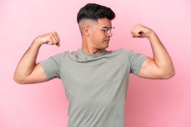 Joven guapo caucásico aislado sobre fondo rosa haciendo gesto fuerte