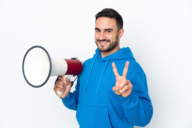 Joven guapo caucásico aislado sosteniendo un megáfono y sonriendo